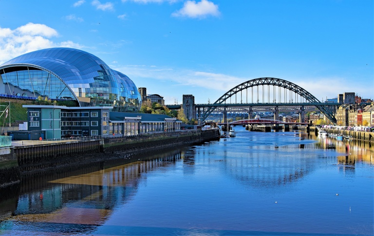 River view with the iconic arched bridge and modern glass building on a sunny day. Reflections dance on the water, creating a serene urban scene.